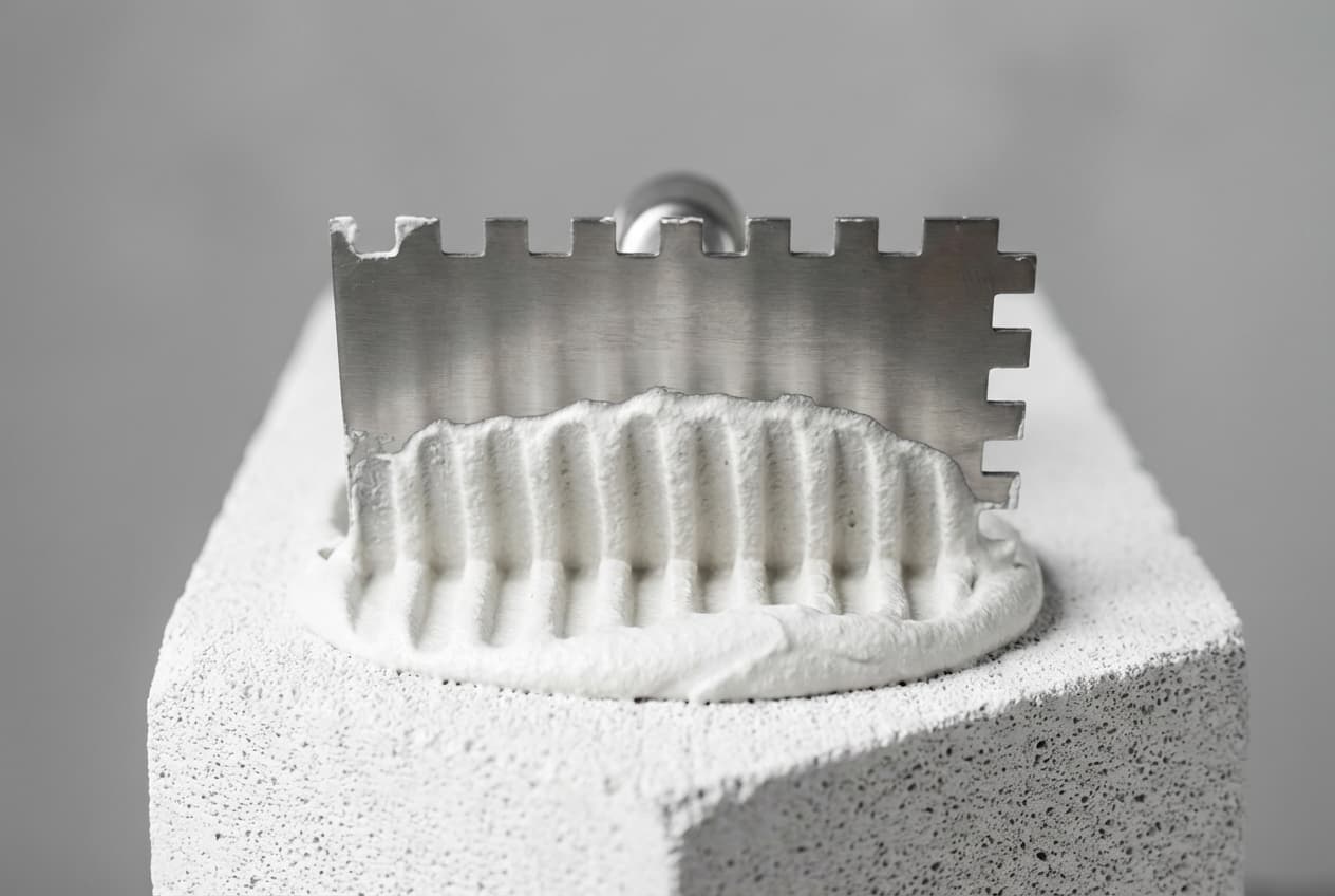 Comment coller du siporex : étapes et matériel nécessaire Gros plan d'un peigne à colle étalant du mortier spécial sur un bloc de Siporex.